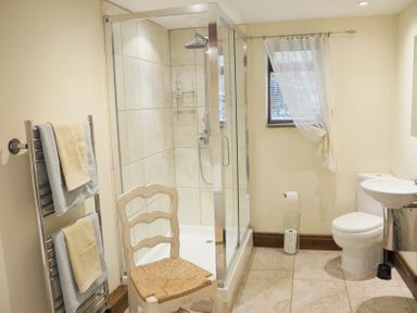 A bathroom with a glass shower enclosure a white chair towels on a towel rack toilet and sink at Bothy Nenthall near Alston