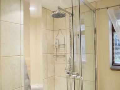 A bathroom corner with a glass shower enclosure a rainfall showerhead and a window with blinds at Bothy Nenthall near Alston