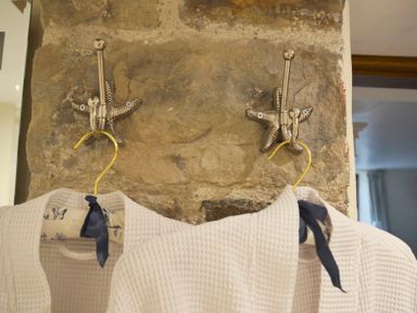 Two white bathrobes hanging on starfish shaped metal hooks attached to a stone wall at Bothy Nenthall near Alston