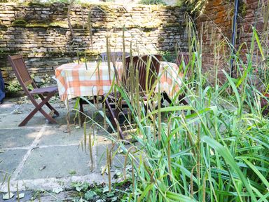 An outdoor patio area with a table covered with a checkered tablecloth and wooden chairs surrounded by stone walls and greenery at Chestnut in Nenthall near Alston
