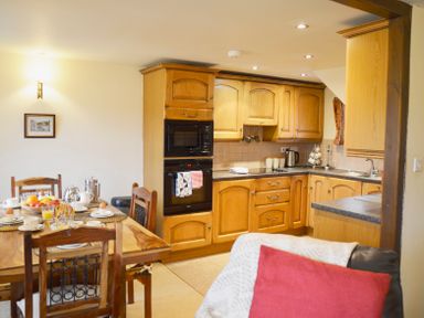 A kitchen with wooden cabinets and a dining table set with breakfast items at Chestnut in Nenthall near Alston