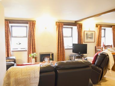 A living room with black leather sofas a TV on a stand and a dining table with chairs at Chestnut in Nenthall near Alston