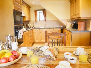 A kitchen with wooden cabinets a table set with juice bread eggs cups and a bowl of fruit at Chestnut in Nenthall near Alston