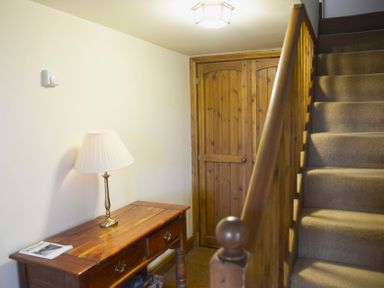 A hallway with a wooden table and lamp a wooden door and carpeted stairs at Chestnut in Nenthall near Alston