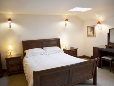 A bedroom with a double bed bedside tables with lamps a dressing table and mirror on white walls at Chestnut in Nenthall near Alston