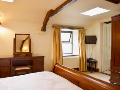A bedroom with a wooden dressing table mirror bed window with curtains and a small wall-mounted television at Chestnut in Nenthall near Alston