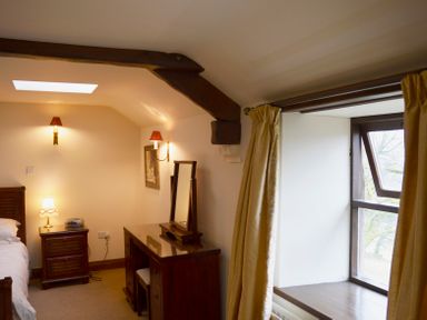 A bedroom with wooden furniture a dressing table a bedside table with a lamp and a window with curtains at Chestnut in Nenthall near Alston