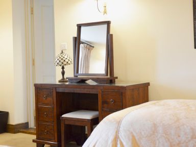 A wooden dressing table with a mirror and a table lamp next to a bed at Chestnut in Nenthall near Alston