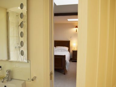 A view through a bathroom door showing a bedroom with a bed and bedside table with a lamp at Chestnut in Nenthall near Alston