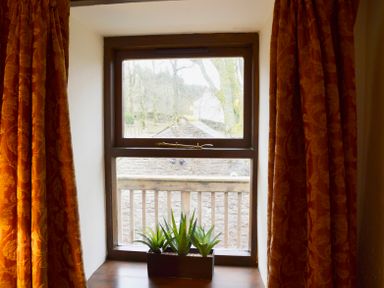 A window with three plants on the sill and orange curtains at Chestnut in Nenthall near Alston