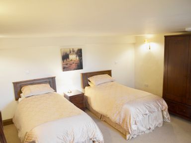 A bedroom with two single beds a bedside table with lamp a painting on the wall and a wooden wardrobe at Chestnut in Nenthall near Alston