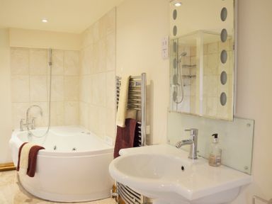 A bathroom with a corner bathtub a sink a mirror and towels at Chestnut in Nenthall near Alston