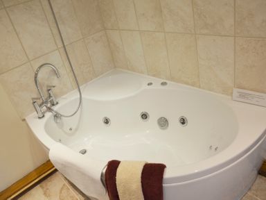 A corner bathtub with chrome faucet and shower head with towels hanging on the side at Chestnut in Nenthall near Alston