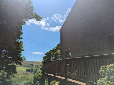 An outdoor view of a balcony attached to a stone building with trees and a grassy hill in the background at Chestnut in Nenthall near Alston
