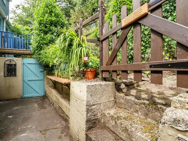 A narrow outdoor area with stone steps and walls wooden gate and blue door with potted plants on the ledge at Vis Valley View in Pentewan