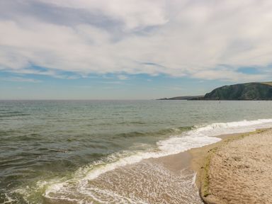A sandy beach with waves coming in and a rocky hill in the distance at Vi's Valley View in Pentewan