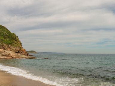 A sandy beach with gentle waves and rocky cliffs covered with greenery at Vi's Valley View in Pentewan