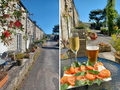 A street view of stone cottages with potted plants and outdoor chairs and a glass table with a plate of tomato and basil salad and two glasses of drink at Vi's Valley View in Pentewan