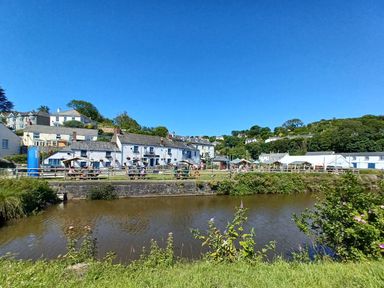 A river with houses and tents on the opposite bank under a clear blue sky at Vi's Valley View in Pentewan