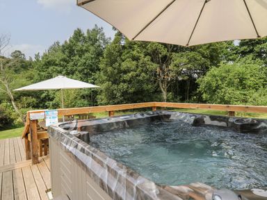 An outdoor hot tub on a wooden deck with umbrellas and trees in the background at Penarth in Cregrina near Builth Wells