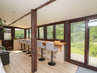 A sunroom with bar stools along a wooden counter by windows and a wooden door at Penarth in Cregrina near Builth Wells