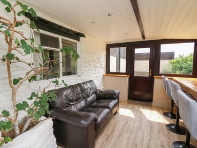 A room with a black leather sofa a potted plant windows and a high wooden table with gray stools at Penarth in Cregrina near Builth Wells