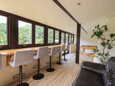 A room with high chairs along a long wooden counter next to windows a black leather sofa and a foosball table at Penarth in Cregrina near Builth Wells