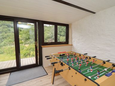 A room with a foosball table near a set of glass doors and windows showing greenery outside at Penarth in Cregrina near Builth Wells