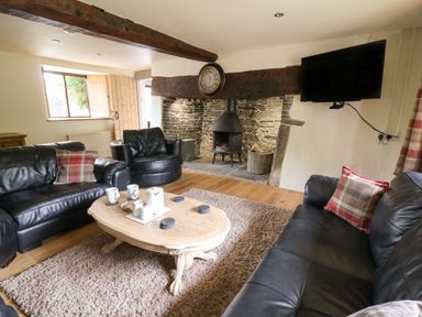 A living room with leather sofas a wooden coffee table a wall clock and a wood burning stove at Penarth in Cregrina near Builth Wells