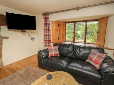 A living room with a black leather sofa with plaid cushions a wall mounted television and a window with wooden shutters at Penarth in Cregrina near Builth Wells