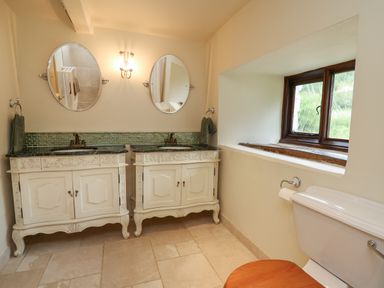 A bathroom with double sinks under oval mirrors and a toilet next to a window at Penarth in Cregrina near Builth Wells