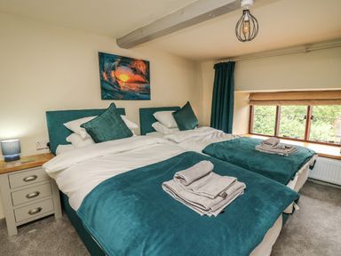 A bedroom with two single beds each with teal bedding and pillows a nightstand with a lamp and a window with a roman shade at Penarth in Cregrina near Builth Wells