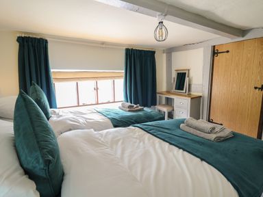A bedroom with two single beds with teal pillows and blankets a window with curtains a wooden door and a dressing table at Penarth in Cregrina near Builth Wells