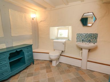 A bathroom with a toilet, pedestal sink, blue mosaic tile backsplash, hexagon mirror, blue cabinet, and small window at Penarth in Cregrina near Builth Wells