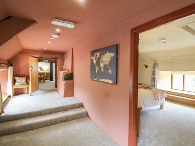 A carpeted hallway with stairs a wooden chair a map on the wall and a view into two bedrooms at Penarth in Cregrina near Builth Wells