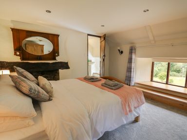 A bedroom with a bed and pillows a wooden-framed mirror and a small window seat at Penarth in Cregrina near Builth Wells