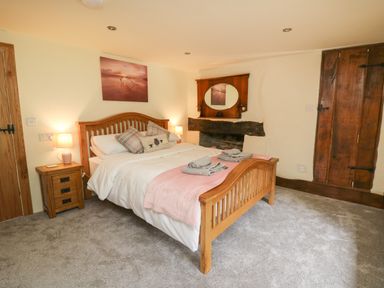 A bedroom with a wooden bed, bedside table with lamp, mirror above a fireplace and wooden doors at Penarth in Cregrina near Builth Wells