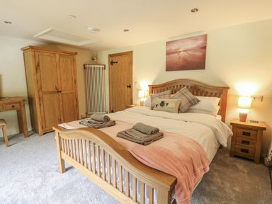 A bedroom with a wooden bed, bedside tables with lamps, a wardrobe, and a desk at Penarth in Cregrina near Builth Wells