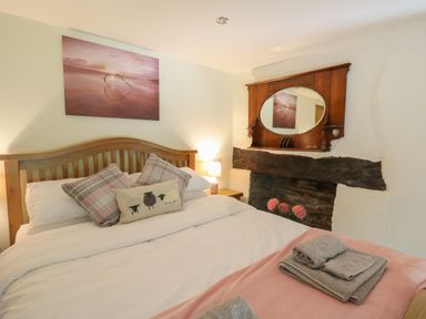 A bedroom with a wooden bed frame, pillows, a lamp on a bedside table, a mirror above a fireplace, and folded towels on the bed at Penarth in Cregrina near Builth Wells
