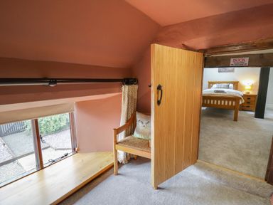 A small seating area with a wooden chair and pillow near a window next to an open wooden door leading to a bedroom at Penarth Cregrina near Builth Wells