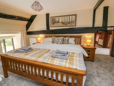 A bedroom with a wooden bed frame a blanket and folded towels on the bed bedside tables with lamps and a window at Penarth in Cregrina near Builth Wells