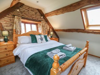 A bedroom with a wooden bed turned posts green pillows white bedding bedside lamps and wooden beams at Penarth Cregrina near Builth Wells