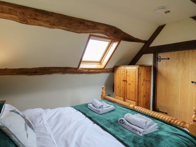 A bedroom with a wooden bed, folded towels on green bedding, a wooden wardrobe, and a skylight window at Penarth in Cregrina near Builth Wells