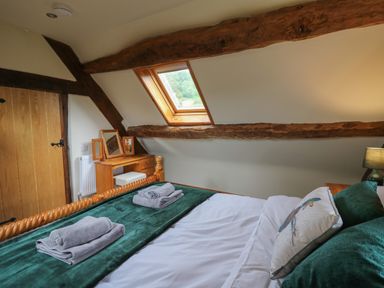 A bedroom with a wooden bed green blanket and folded towels a wooden dressing table and a skylight window at Penarth in Cregrina near Builth Wells