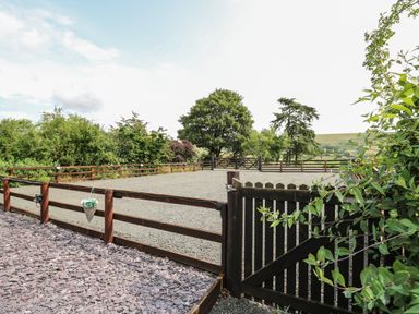 A fenced gravel area with wooden gates and surrounding trees at Penarth in Cregrina near Builth Wells