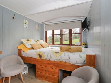 A small bedroom with a bed with sunflower bedding two gray chairs and a wall mounted TV at Rabbit Hill Hut in Govilon