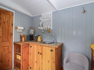 A kitchenette with wooden cabinets a sink a microwave and kitchen utensils at Rabbit Hill Hut in Govilon