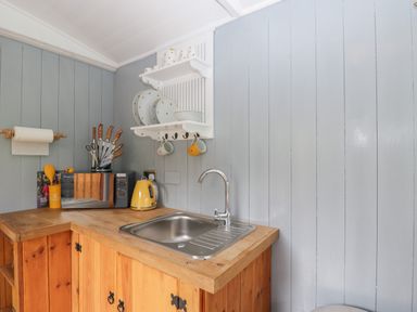A kitchen corner with wooden cabinets a metal sink a microwave yellow kettle and kitchen utensils at Rabbit Hill Hut in Govilon