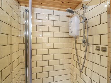 A shower area with beige subway tiles a mounted shower unit and a wooden ceiling at Rabbit Hill Hut in Govilon
