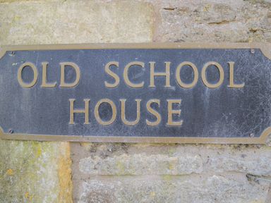 A close up of a black and gold sign on a stone wall that reads Old School House at The Old School House in Lower Swell near Stow-On-The-Wold